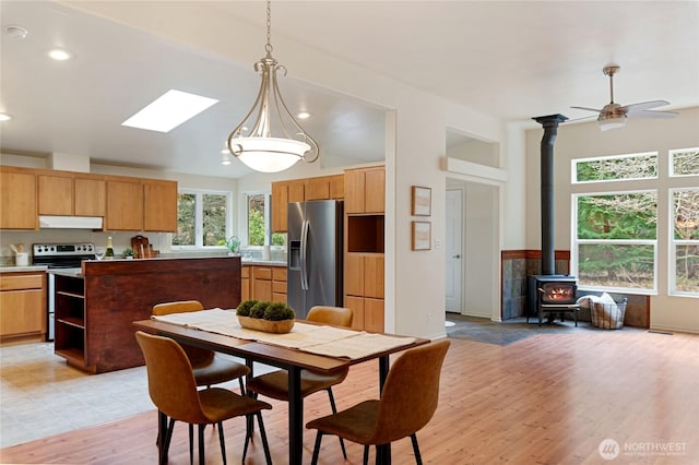 kitchen with under cabinet range hood, pendant lighting, light wood-type flooring, vaulted ceiling with skylight, and appliances with stainless steel finishes