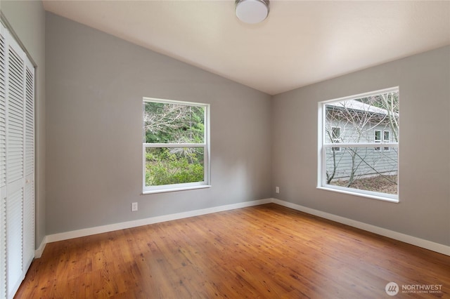 unfurnished bedroom with lofted ceiling, wood finished floors, baseboards, and a closet