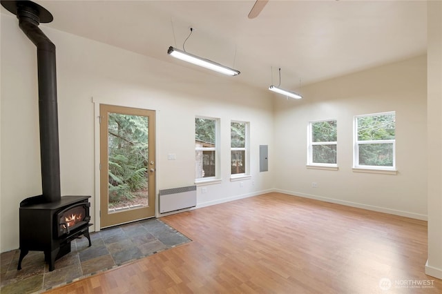 interior space with radiator, wood finished floors, baseboards, a wood stove, and electric panel