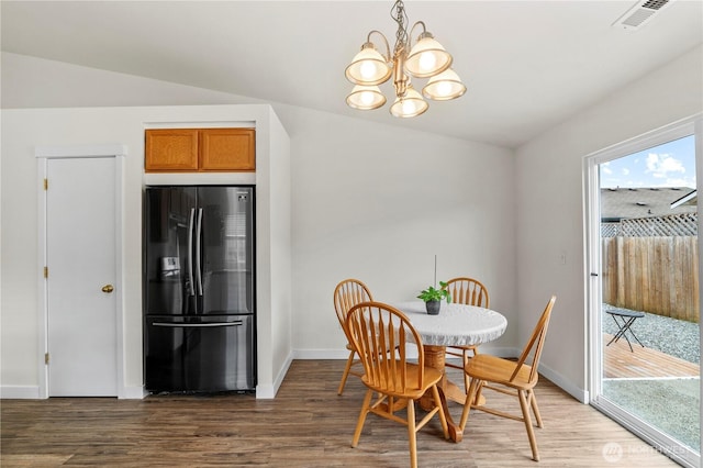 dining space with visible vents, wood finished floors, baseboards, a chandelier, and vaulted ceiling