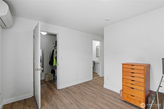 unfurnished bedroom featuring light wood finished floors, a walk in closet, baseboards, a closet, and a wall mounted AC