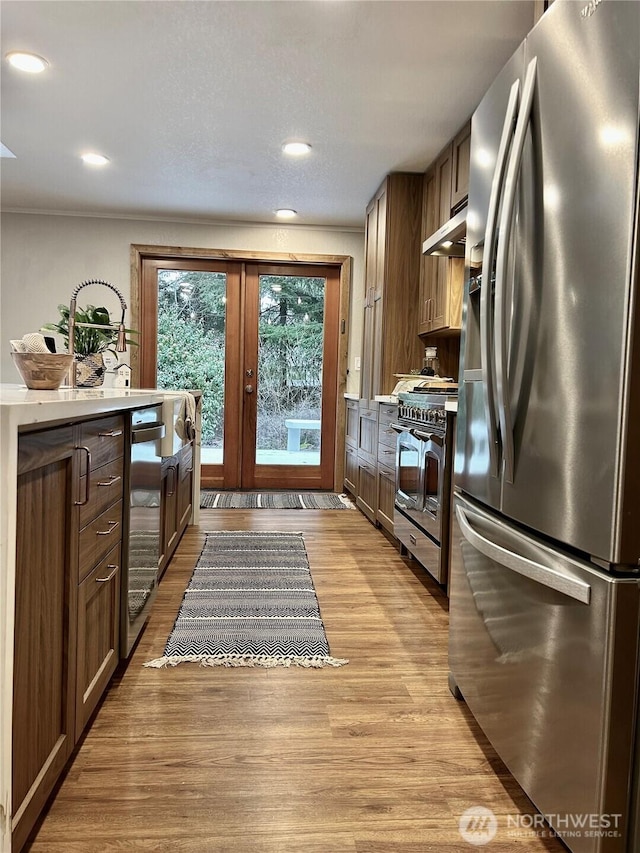 kitchen featuring under cabinet range hood, light wood-style flooring, light countertops, and appliances with stainless steel finishes