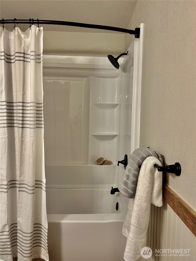 bathroom with a textured wall and shower / bath combo