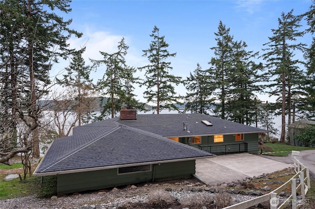 view of side of property with a patio area, a chimney, and a shingled roof