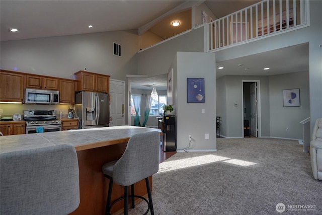 kitchen with visible vents, carpet floors, a breakfast bar, stainless steel appliances, and brown cabinets