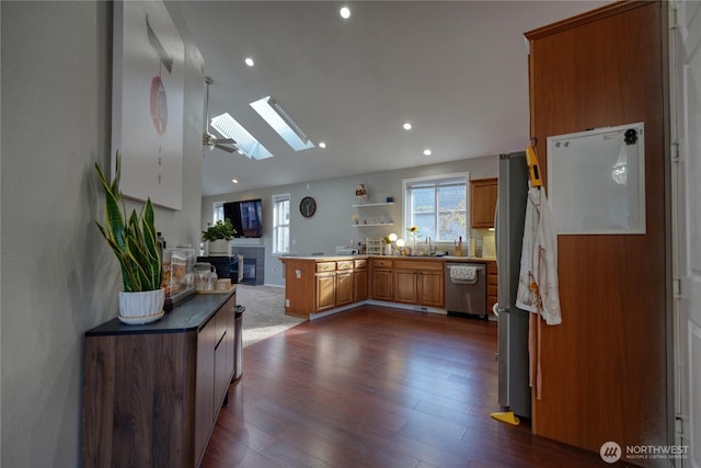 kitchen with vaulted ceiling with skylight, a peninsula, brown cabinetry, dishwasher, and dark wood-style flooring