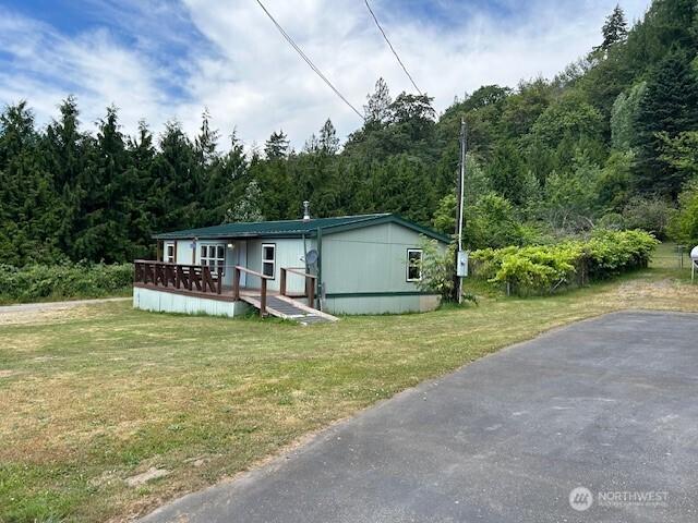 manufactured / mobile home featuring a wooded view, a wooden deck, and a front yard