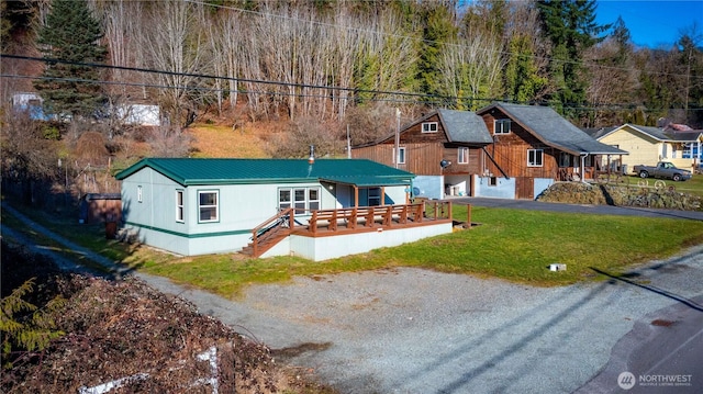 view of front facade with a deck, aphalt driveway, metal roof, a front yard, and a garage