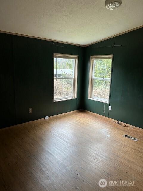 empty room with vaulted ceiling, visible vents, a textured ceiling, and wood finished floors