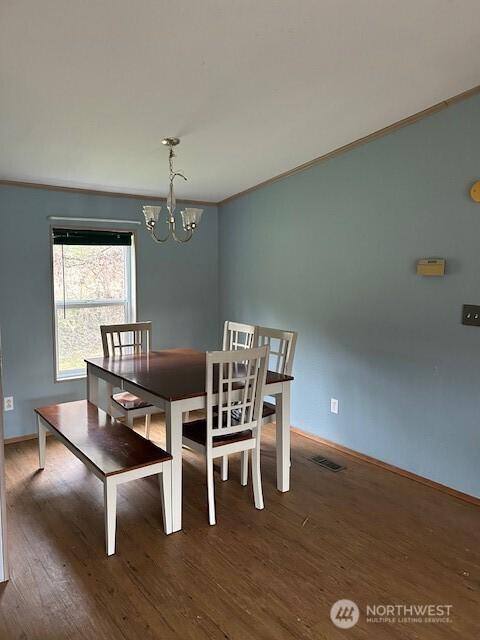 dining space featuring visible vents, crown molding, baseboards, an inviting chandelier, and wood finished floors