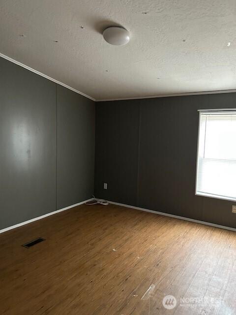 spare room featuring visible vents, ornamental molding, a textured ceiling, and wood finished floors