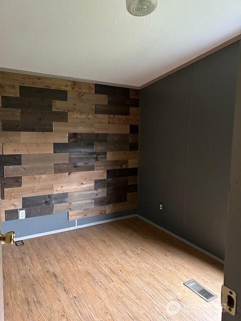 spare room with visible vents, crown molding, wooden walls, and wood finished floors