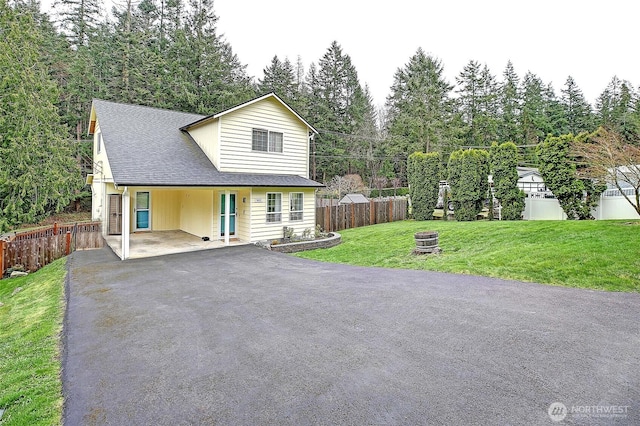 view of front facade featuring fence, driveway, a shingled roof, a front lawn, and a carport