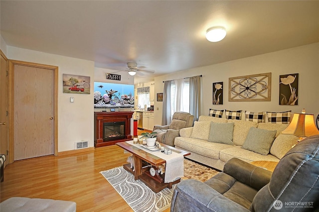 living room with visible vents, a glass covered fireplace, a ceiling fan, and light wood finished floors