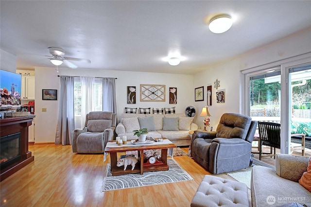 living room featuring light wood-style floors, a glass covered fireplace, and a ceiling fan