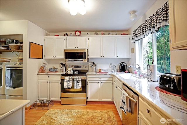 kitchen with washer and clothes dryer, a sink, stainless steel appliances, light wood-style floors, and light countertops