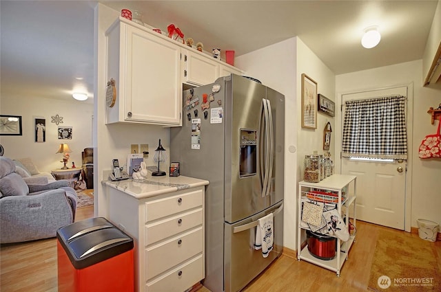 kitchen featuring light wood finished floors, light countertops, stainless steel fridge, white cabinetry, and open floor plan