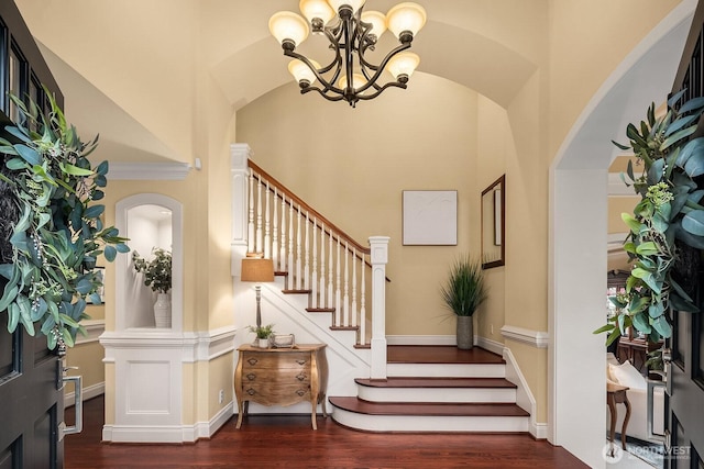 entryway featuring baseboards, a chandelier, stairway, lofted ceiling, and wood finished floors