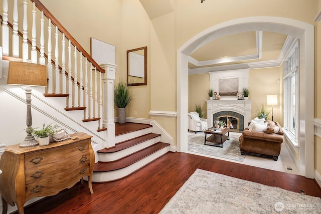 interior space with stairway, wood finished floors, arched walkways, a glass covered fireplace, and crown molding