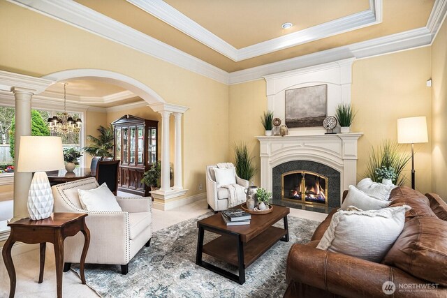 living room with a tray ceiling, decorative columns, arched walkways, an inviting chandelier, and a premium fireplace