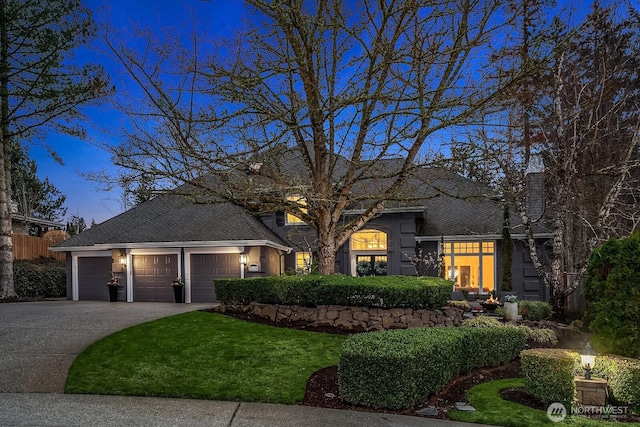 view of front facade featuring a shingled roof, concrete driveway, a garage, and a front lawn