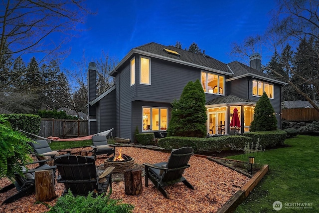 back of property with a chimney, a fire pit, and fence