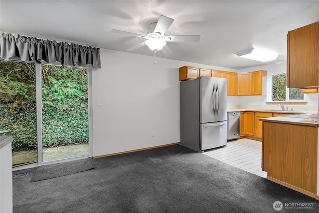 kitchen featuring a sink, appliances with stainless steel finishes, light countertops, baseboards, and light colored carpet