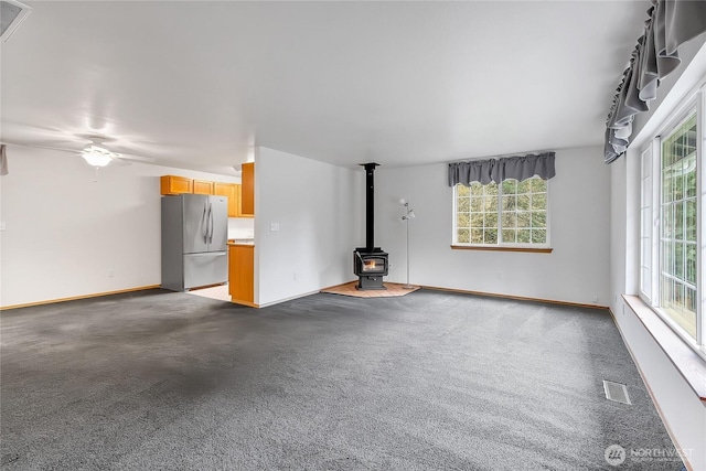 unfurnished living room with visible vents, baseboards, a wood stove, and a ceiling fan