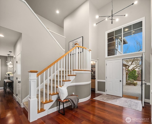 entrance foyer featuring hardwood / wood-style floors, a towering ceiling, baseboards, a chandelier, and stairs