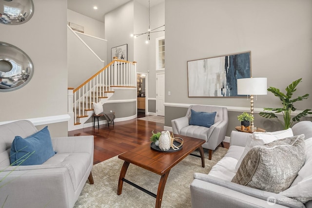 living area featuring stairway, wood finished floors, baseboards, a towering ceiling, and a notable chandelier