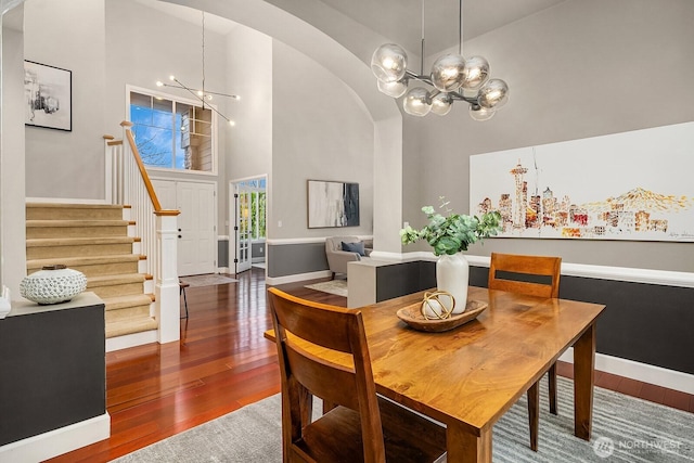 dining space with arched walkways, a notable chandelier, high vaulted ceiling, and hardwood / wood-style flooring