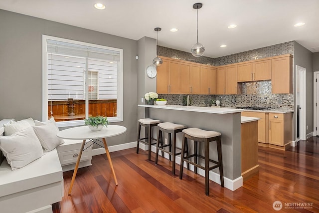 kitchen with a kitchen bar, light brown cabinetry, dark wood-style flooring, and light countertops