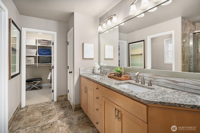 bathroom featuring double vanity, a shower stall, a spacious closet, and a sink