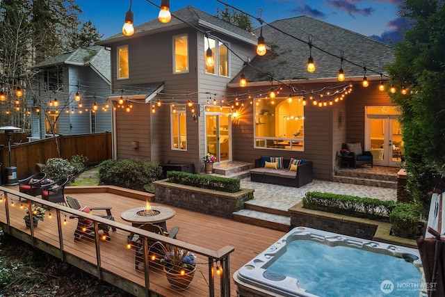 back of house featuring fence, roof with shingles, an outdoor living space with a fire pit, a deck, and hot tub deck surround