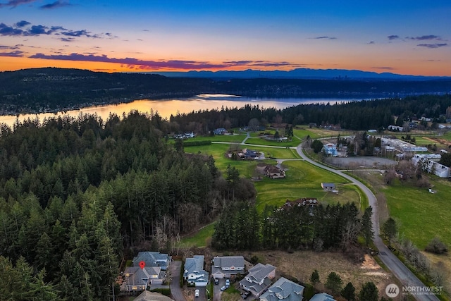 aerial view at dusk featuring a water and mountain view and a wooded view