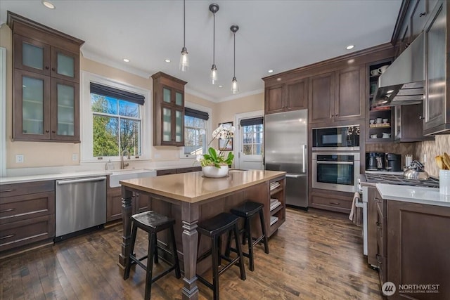 kitchen with a kitchen island, a sink, light countertops, built in appliances, and crown molding