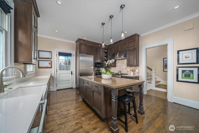 kitchen featuring dark wood-type flooring, under cabinet range hood, dark brown cabinetry, light countertops, and built in appliances