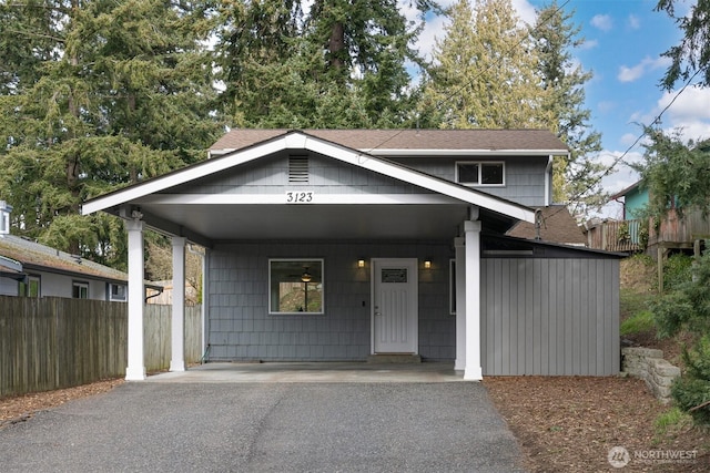 view of front of home featuring aphalt driveway, an attached carport, a shingled roof, and fence