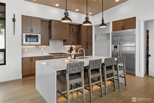 kitchen with light wood-type flooring, light countertops, appliances with stainless steel finishes, pendant lighting, and tasteful backsplash