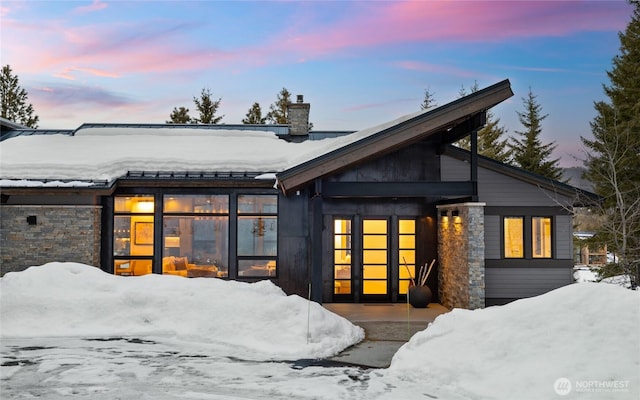 snow covered rear of property featuring a chimney