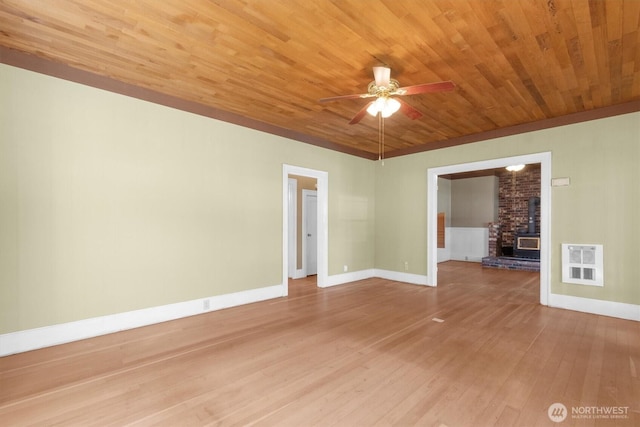 empty room with wood finished floors, wood ceiling, a ceiling fan, baseboards, and a wood stove