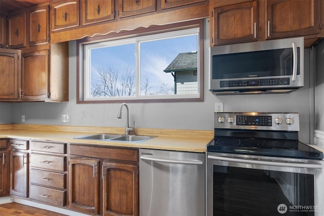 kitchen with brown cabinetry, stainless steel appliances, a sink, and light countertops