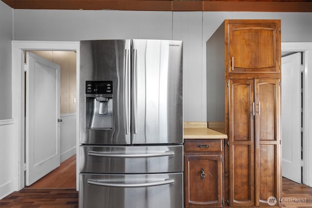 kitchen with light countertops, dark wood-type flooring, brown cabinetry, and stainless steel refrigerator with ice dispenser