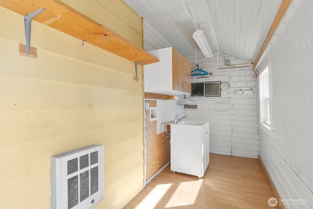 laundry room with heating unit, cabinet space, light wood-type flooring, and a sink