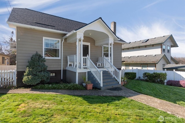 view of front of house featuring a porch, a shingled roof, fence, a front lawn, and a chimney