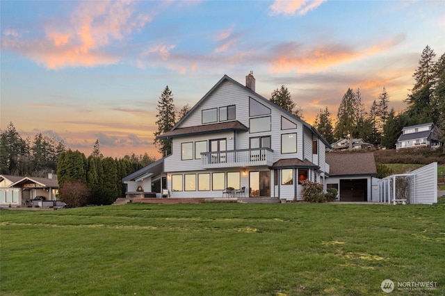 back of property at dusk featuring a balcony, a chimney, an attached garage, and a lawn