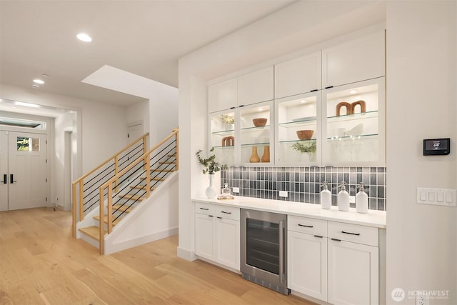 bar featuring light wood-style floors, wine cooler, tasteful backsplash, and stairs