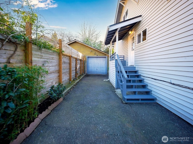 view of property exterior with driveway, a detached garage, an outdoor structure, and fence