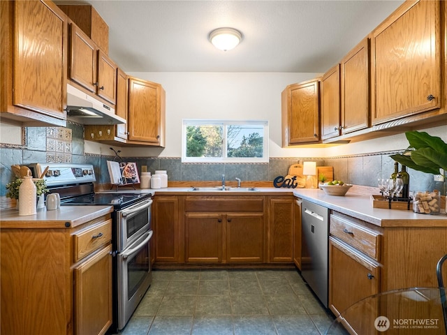 kitchen with under cabinet range hood, a sink, stainless steel appliances, brown cabinetry, and light countertops