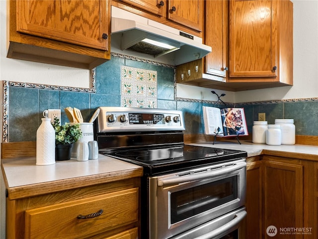 kitchen featuring under cabinet range hood, double oven range, tasteful backsplash, and light countertops